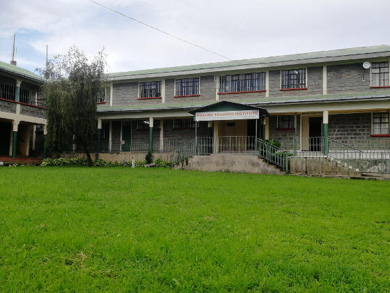 A lawn leading to the entrance to a wide grey building